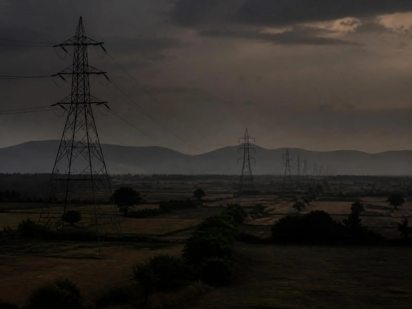 Transmission pylons crossing farmland at dusk